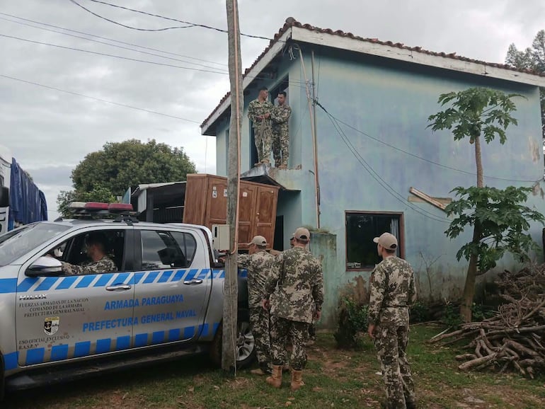 Cinco miembros de la Armada Paraguaya en uniforme camuflado observan desde el techo de una casa azul, con cielo nublado de fondo.