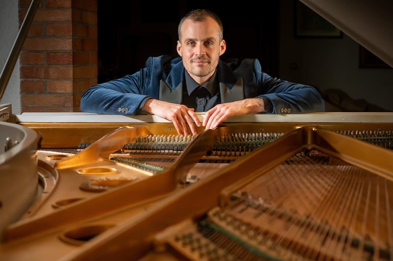 Hombre sonriente con chaqueta oscura sobre un piano elegante en ambiente con luz suave.