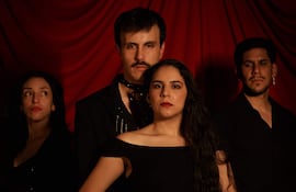 Cuatro miembros del elenco, dos mujeres con vestidos oscuros y dos hombres con atuendos serios, en un fondo de tela roja.