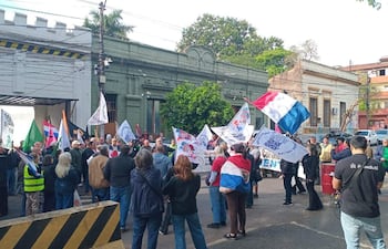 Grupo de manifestantes sosteniendo banderas y pancartas en un entorno urbano con edificios clásicos de fondo.