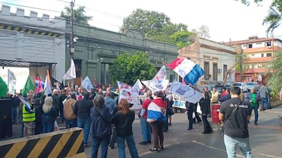Grupo de manifestantes sosteniendo banderas y pancartas en un entorno urbano con edificios clásicos de fondo.