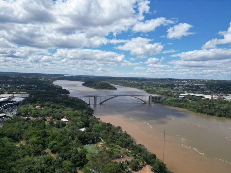 Vista aérea de un río marrón rodeado de vegetación y un puente moderno, sin personas visibles en la escena.