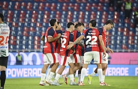 Jugadores de Cerro Porteño vestidos de rojo y azul celebran un gol, rodeando a uno de sus compañeros en un ambiente festivo.