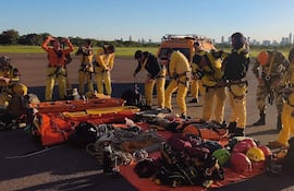 Grupo de bomberos en uniformes amarillos y naranjas, ajustando arneses y equipos sobre una lona naranja.