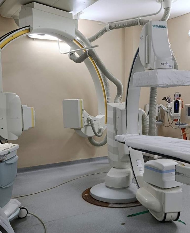 Sala de procedimientos médicos con equipos de imagenología Siemens y camilla blanca, sin personas visibles.
