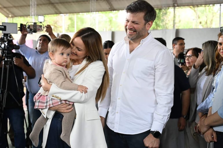 Soledad Núñez sonríe mientras sostiene a una niña, con Bruno Defelippe a su lado, en un evento electoral formal.