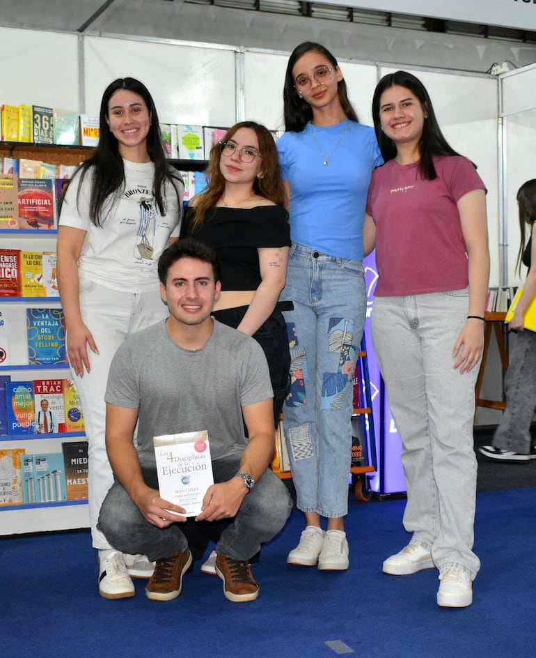 Cuatro mujeres y un hombre sonríen en la feria, rodeados de estantes llenos de libros.