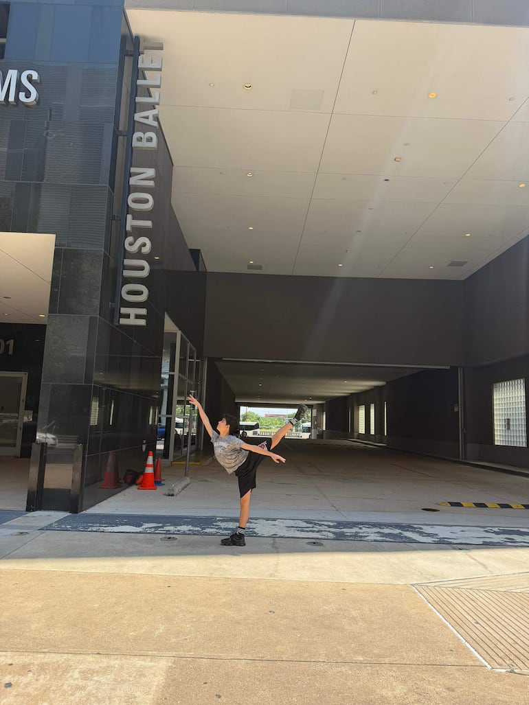 Niño de 10 a 12 años en camiseta gris y pantalones cortos negros, bailando frente al edificio del Houston Ballet.