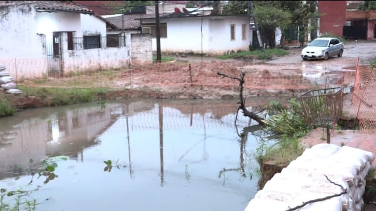 Sin personas visibles. Estanque de agua y coche blanco estacionado en área de obras con malla de seguridad. Sacos de arena alineados.