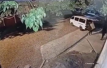 Dos individuos de ropa oscura en cerca de una furgoneta blanca en un entorno nocturno y de vegetación.