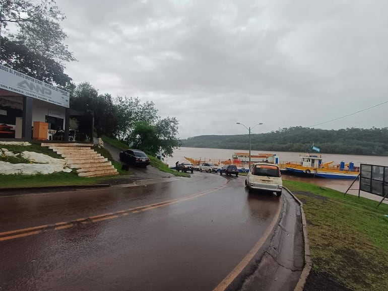 Un puerto con un camino mojado, vehículos estacionados y un ferry atracado, en un día nublado y húmedo.