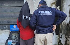 Dos personas en entorno urbano: un agente con chaqueta 'POLICÍA' y un detenido cubierto con saco negro.