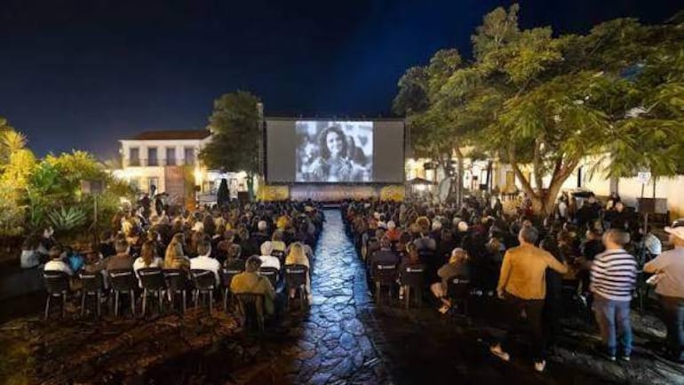 Grupo de personas sentadas frente a una pantalla grande, disfrutando de una película en un ambiente urbano nocturno.