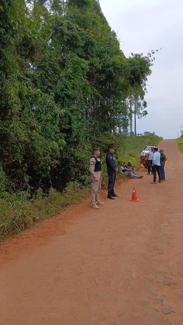 Agentes de seguridad en uniforme militar y policial monitorean a un grupo de personas en un sendero rodeado de vegetación, bajo un cielo nublado.