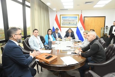 Latorre Martínez en traje conversando mientras Centurión González y Meza lo observan. Fondo con banderas de Paraguay y documentos sobre la mesa.