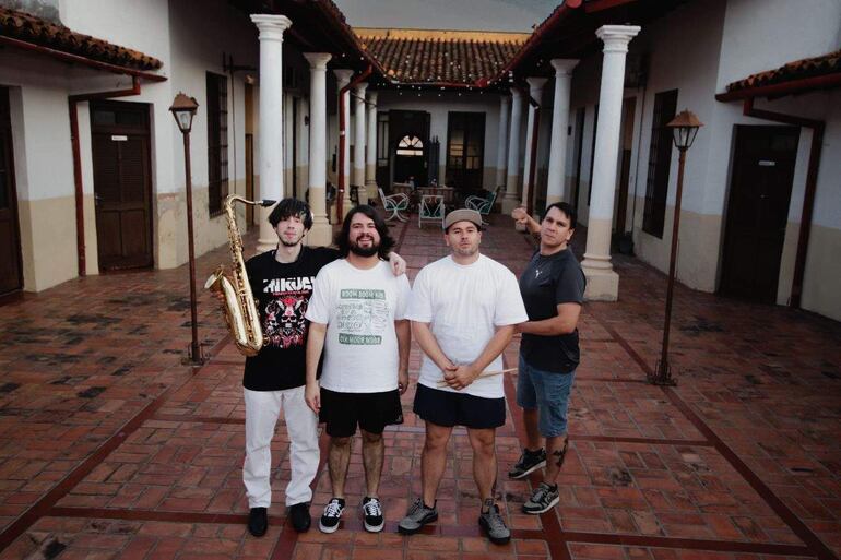 Cuatro hombres de Vecindad Autopsia, con camisetas y pantalones cortos, posan sonrientes en un entorno al aire libre.