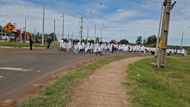 Grupo de bioquímicos en batas blancas marchan con globos azules y una bandera de Paraguay en la rotonda de Coronel Oviedo.