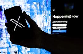 Un usuario sostiene un teléfono móvil que muestra el logotipo 'X' frente a la página principal de Twitter.