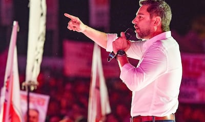 Pedro Alliana, enérgico y con camisa blanca, se dirige al público con micrófono en mano, rodeado de banderas en un evento al aire libre.