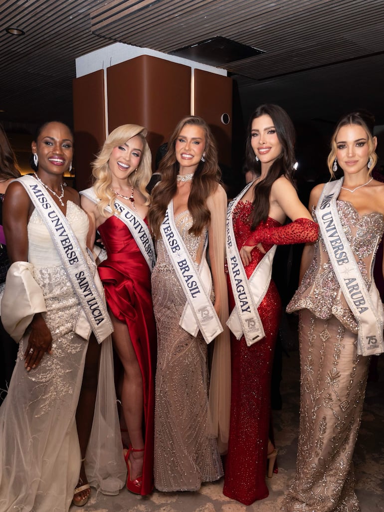 Cinco mujeres en vestidos elegantes sonríen, con bandas que indican sus países en un ambiente formal y decorado.