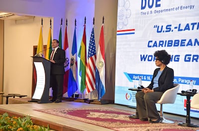 Félix Sosa en podio con traje oscuro, mientras mujer con auriculares lo escucha atentamente, rodeados de banderas de países americanos.
