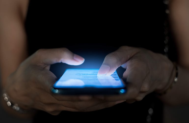 Dos manos sosteniendo un teléfono móvil encendido en un entorno oscuro, enfocándose en la interacción digital.