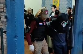 Agente en chaleco táctico sostiene a un hombre cabizbajo en un entorno cerrado, reflejando una situación de control de seguridad.