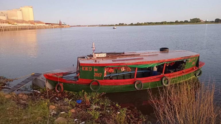 Embarcación verde 'KIKO' amarrada en la orilla, con muelle cercano y basura visible en un ambiente tranquilo y natural.