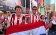 Tres jóvenes, con camisetas rojas y blancas, sostienen una bandera de Paraguay en un ambiente festivo de Times Square.