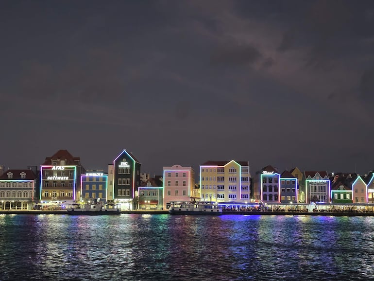 Paísaje costero nocturno en Curazao con casas coloniales brillantes en tonos azul, amarillo, rosa y verde.