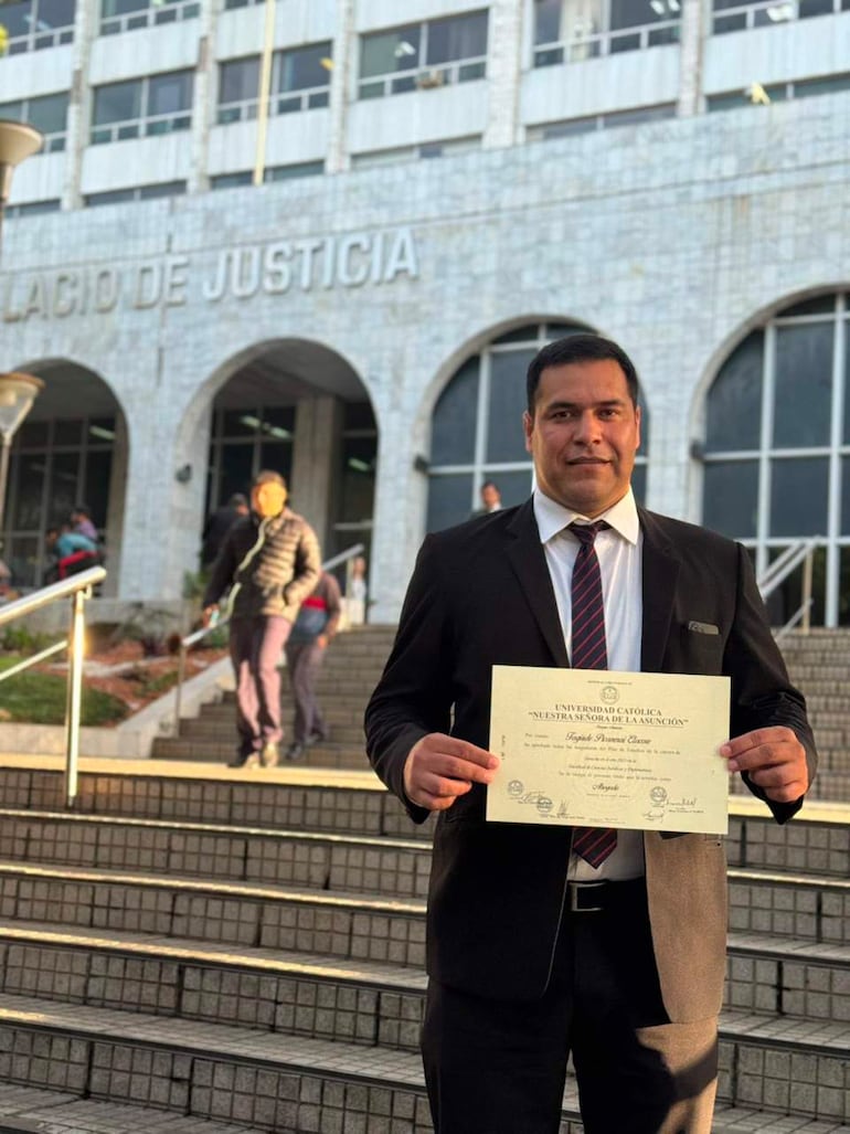 Hombre de pie en escalinata del Palacio de Justicia, vistiendo traje oscuro y sosteniendo diploma con sonrisa.