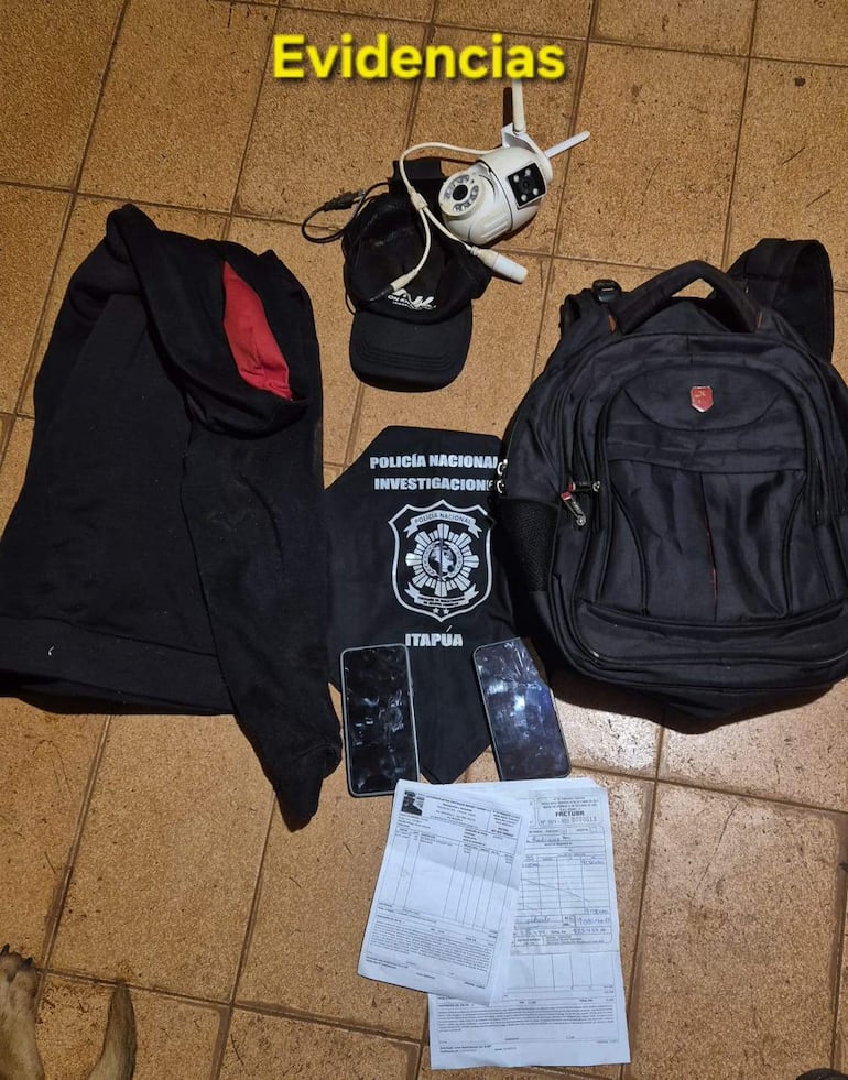 Elementos de investigación policial dispuestos sobre el suelo, incluyendo sudadera negra y dos teléfonos móviles dañados.