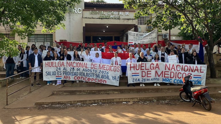 Grupo de médicos y personal de salud con batas blancas y pancartas frente al Hospital Regional, mostrando determinación y unidad.