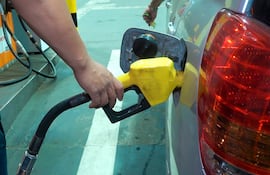 Una persona carga gasolina en una estación de servicio mientras sostiene un billete para el pago.