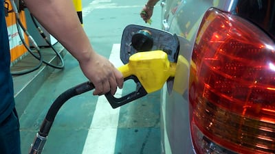 Persona con manguera amarilla de combustible en mano, en una estación de servicio con dispensadores visibles de fondo.