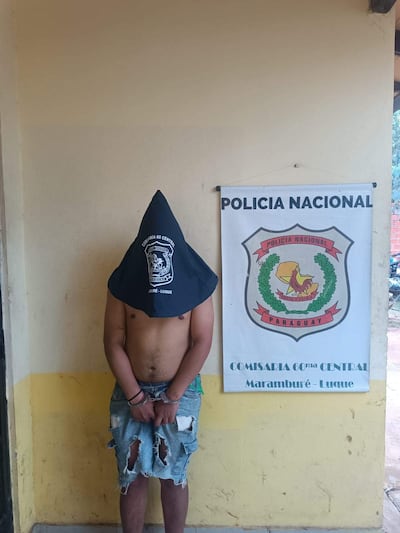 Hombre con gorro negro, pantalón de mezclilla roto y esposado, frente a la comisaría 60ma de Luque.