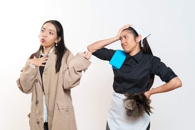 Mujeres en escena: una en chaqueta beige con gesto de sorpresa, otra en blusa negra lidiando con utensilios de limpieza.