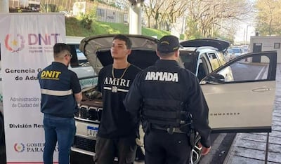 Uniformados del DNIT y la Armada observan un vehículo con capó abierto, mientras un joven con camiseta negra se muestra serio.