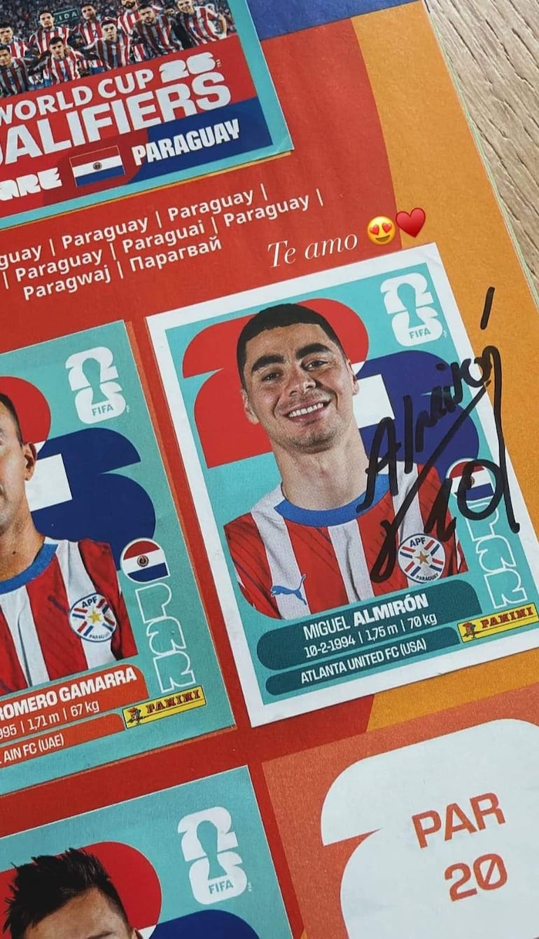 Miguel Almirón sonríe mientras lleva la camiseta de Paraguay, sentado entre tarjetas de colección de futbolistas con colores rojo, blanco y azul.