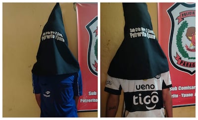 Dos jóvenes de espaldas con capuchas, uno en camiseta azul y otro en blanca, en un ambiente policial con cartel de identificación.
