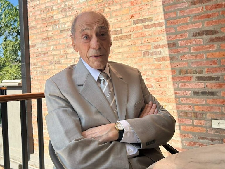Eugenio Raúl Zaffaroni, vestido con traje claro y corbata a rayas, sentado con expresión seria en un entorno acogedor.