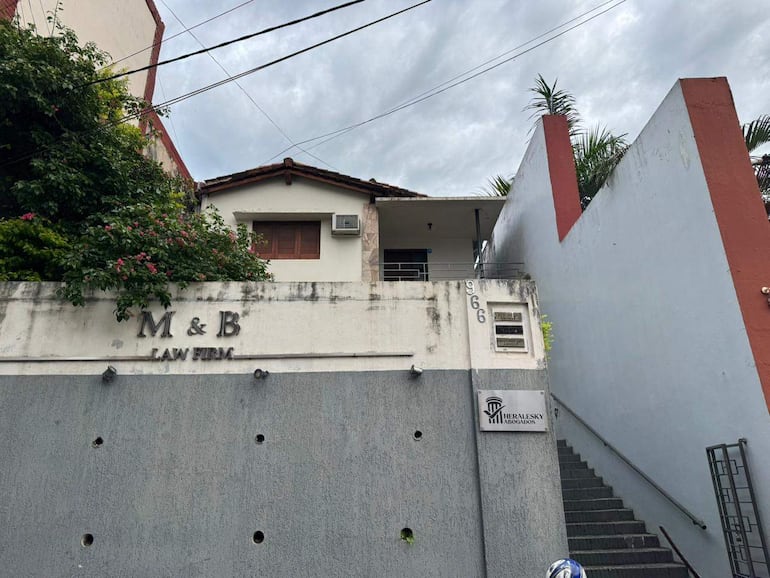 Fachada del edificio de la firma M & B LAW FIRM, con vegetación y escaleras de acceso en un día nublado.