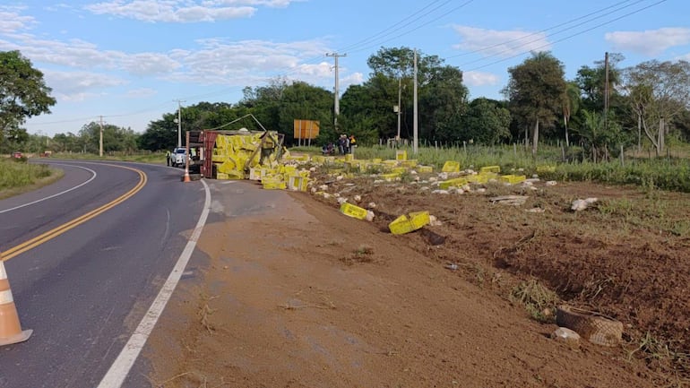 Tres hombres en ropa reflectante observan un camión volcado en la carretera, rodeado de canastas amarillas y vegetación.