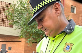 Hombre con uniforme de PMT, camisa amarilla y gris, sostiene un celular y un documento en una calle urbana.