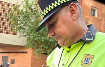 Hombre con uniforme de PMT, camisa amarilla y gris, sostiene un celular y un documento en una calle urbana.