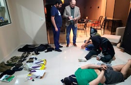 El fiscal Lorenzo Lezcano (con saco) y el subcomisario David Delgado (con remera) conversan cerca de los tres miembros del PCC detenidos, quienes aparecen esposados en el suelo de un duplex en Lambaré, donde detectaron preparativos para un atentado en la fiesta El Retrovisor.