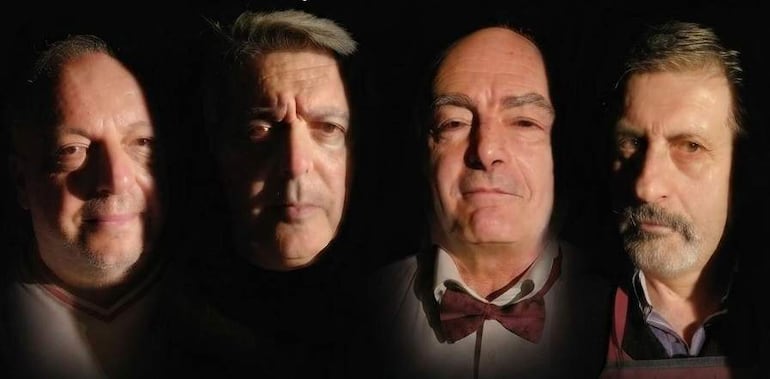Cuatro hombres posan en un estudio oscuro, mostrando diferentes expresiones y rostros iluminados por luces suaves.