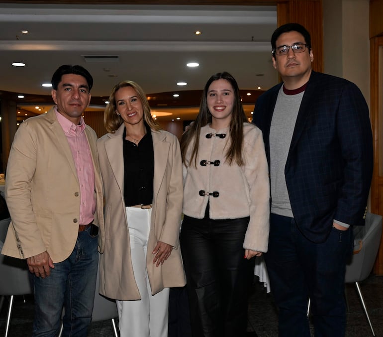 Hombre de camisa rosa y chaqueta beige sonríe junto a mujer con abrigo claro; joven sonriente y hombre serio con gafas en salón.