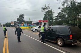 Dos policías con uniforme oscuro y chalecos reflectantes conversan con un conductor en un vehículo negro en una carretera nublada.