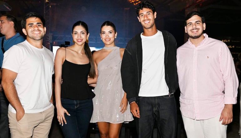 Cinco personas sonrientes en evento festivo, con una mujer en vestido brillante en el centro y un hombre en camisa de rayas a la derecha.